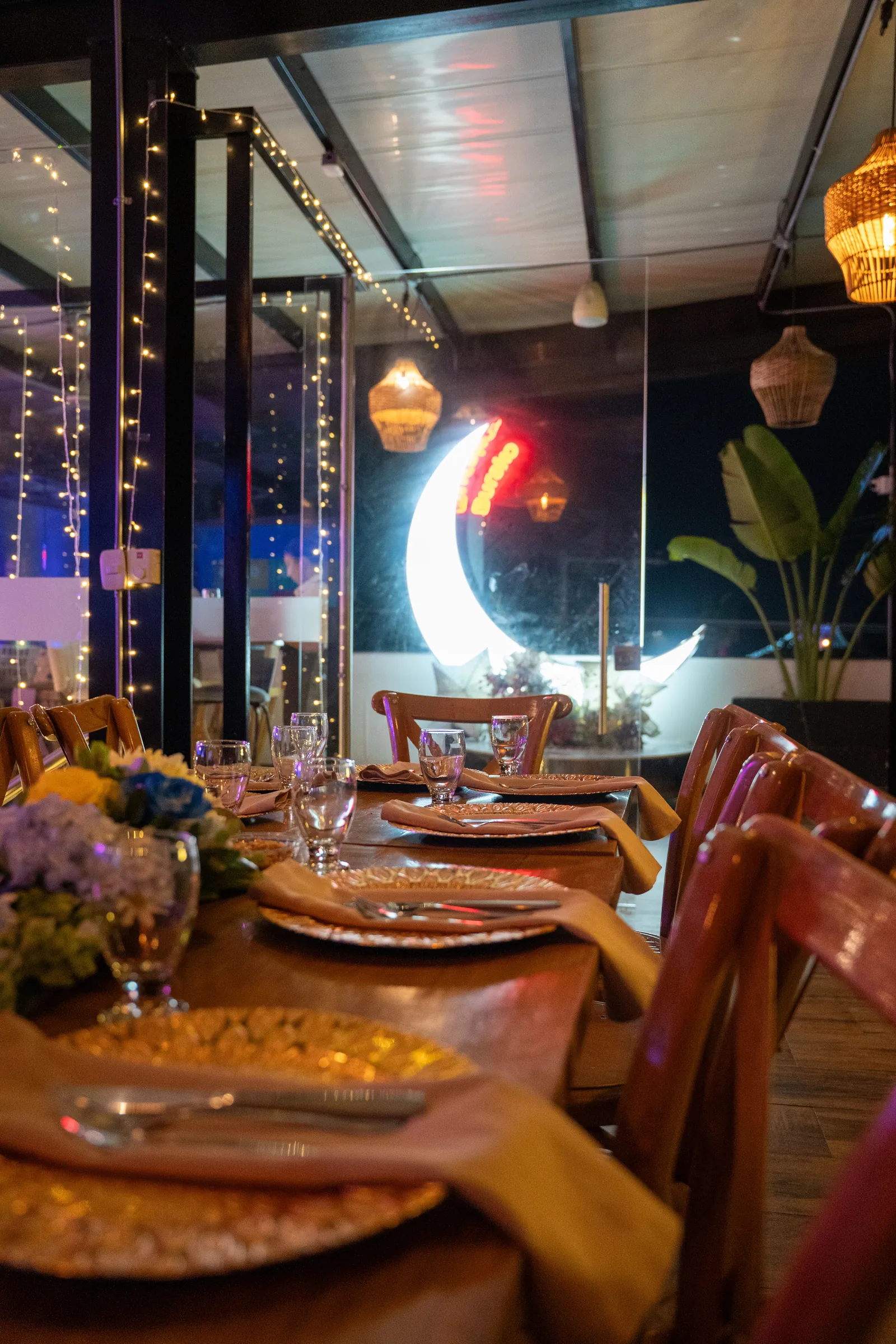 Terraza principal de Burako Gourmet Bar de noche, mesas dispuestas junto a la luna de neón